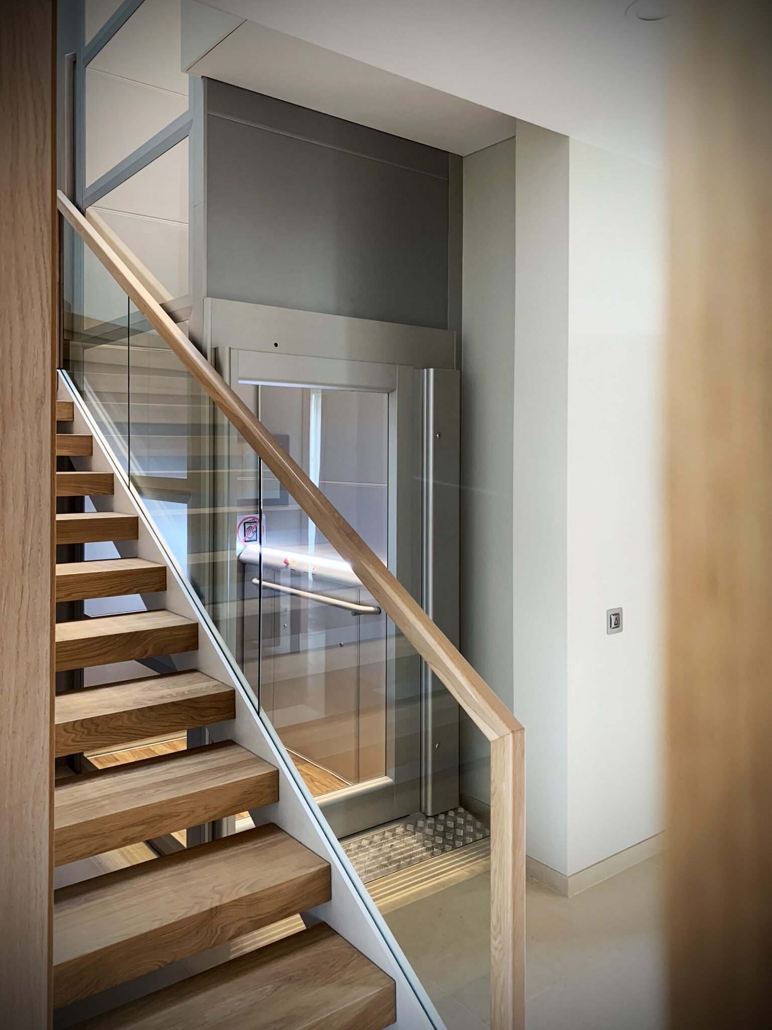 Design huislift met glazen deur naast een houten trap